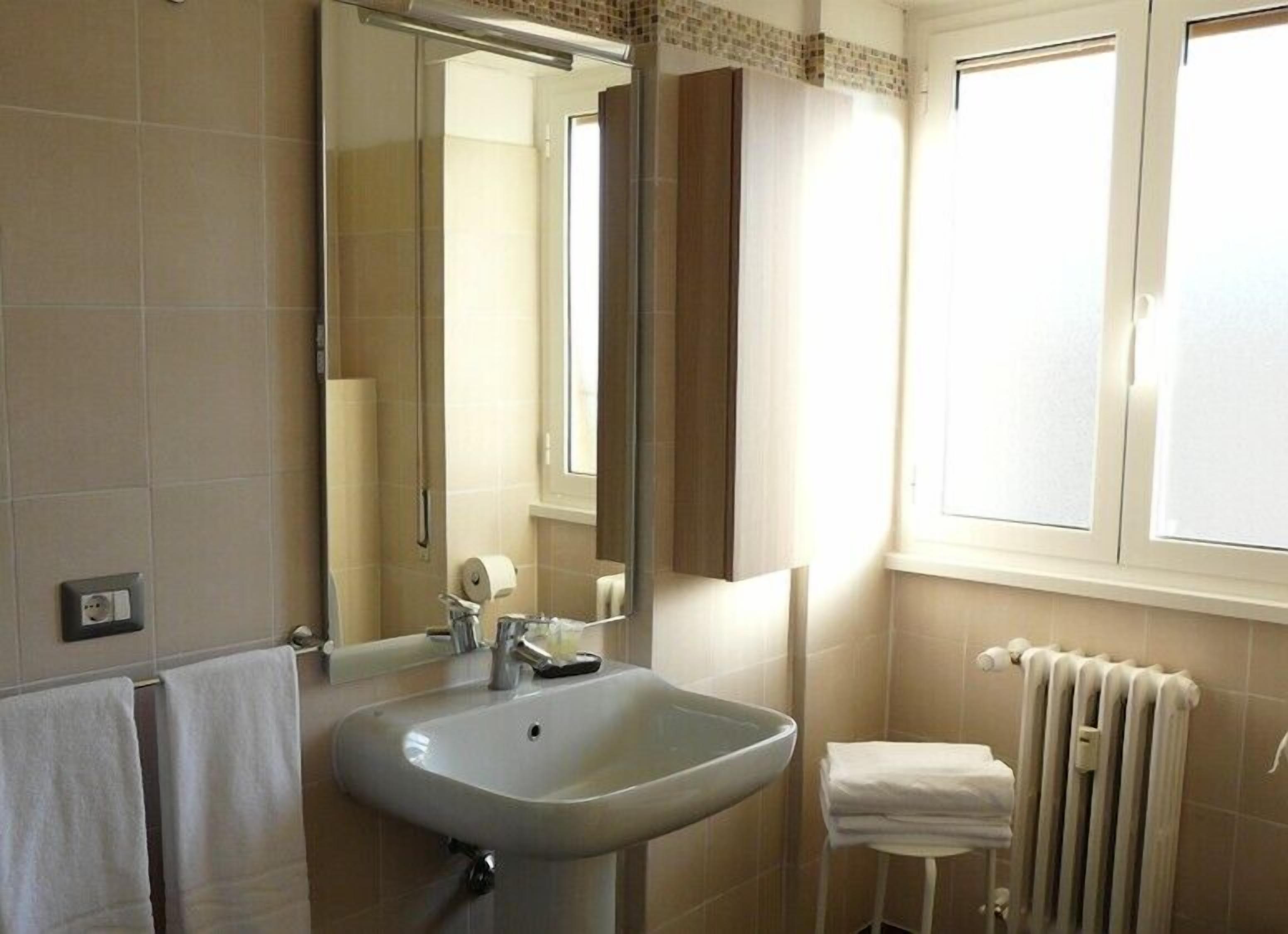 Un baño con lavamanos, espejo, toallero y radiador.