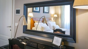 A hotel room with a large mirror, a bed with white linens, two bedside lamps, a remote control, and a small desk with a cup and a menu. - Villino Fiorentino (Florence)