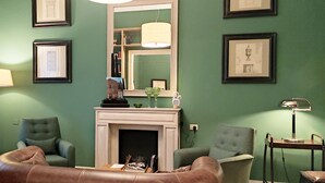 A living room with a fireplace, green walls, framed pictures, and two armchairs. - Villino Fiorentino (Florence)