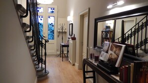 A hallway with a staircase, a door with stained glass, a table with books and a framed picture, and a bookshelf in the background. - Villino Fiorentino (Florence)