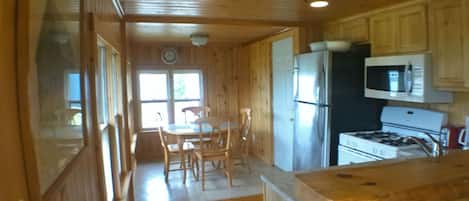 A wooden cabin interior with a kitchen area, dining table, and chairs.