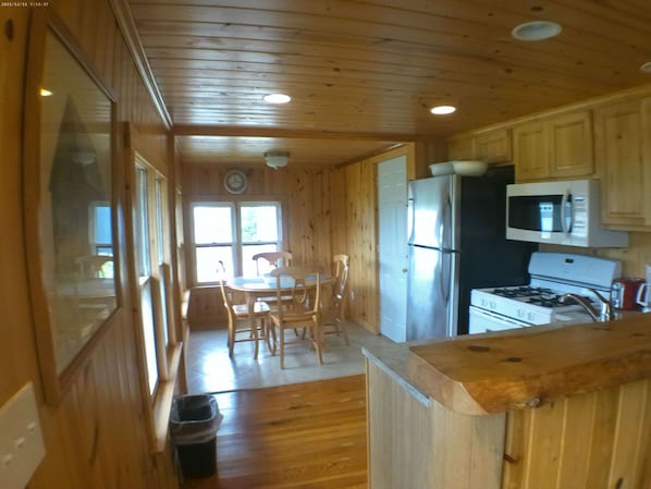 A wooden cabin interior with a kitchen area, dining table, and chairs. - Crystal Lake Resort (Beulah)