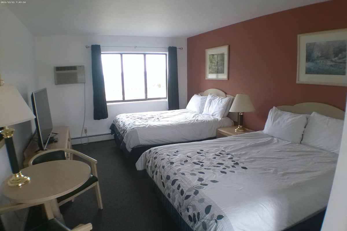 Une chambre d’hôtel avec deux lits, un bureau, une chaise, une lampe et une fenêtre avec des rideaux.