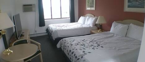 Ein Hotelzimmer mit zwei Betten, einem Schreibtisch, einem Stuhl, einer Lampe und einem Fenster mit Vorhängen.