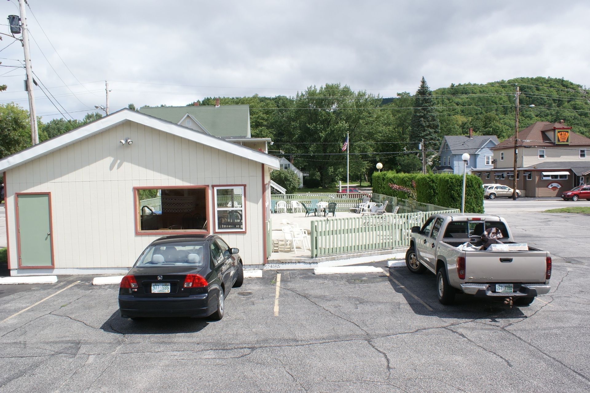 A small building with a green door and a window, a parking lot with two cars, and a hill with trees in the background.
