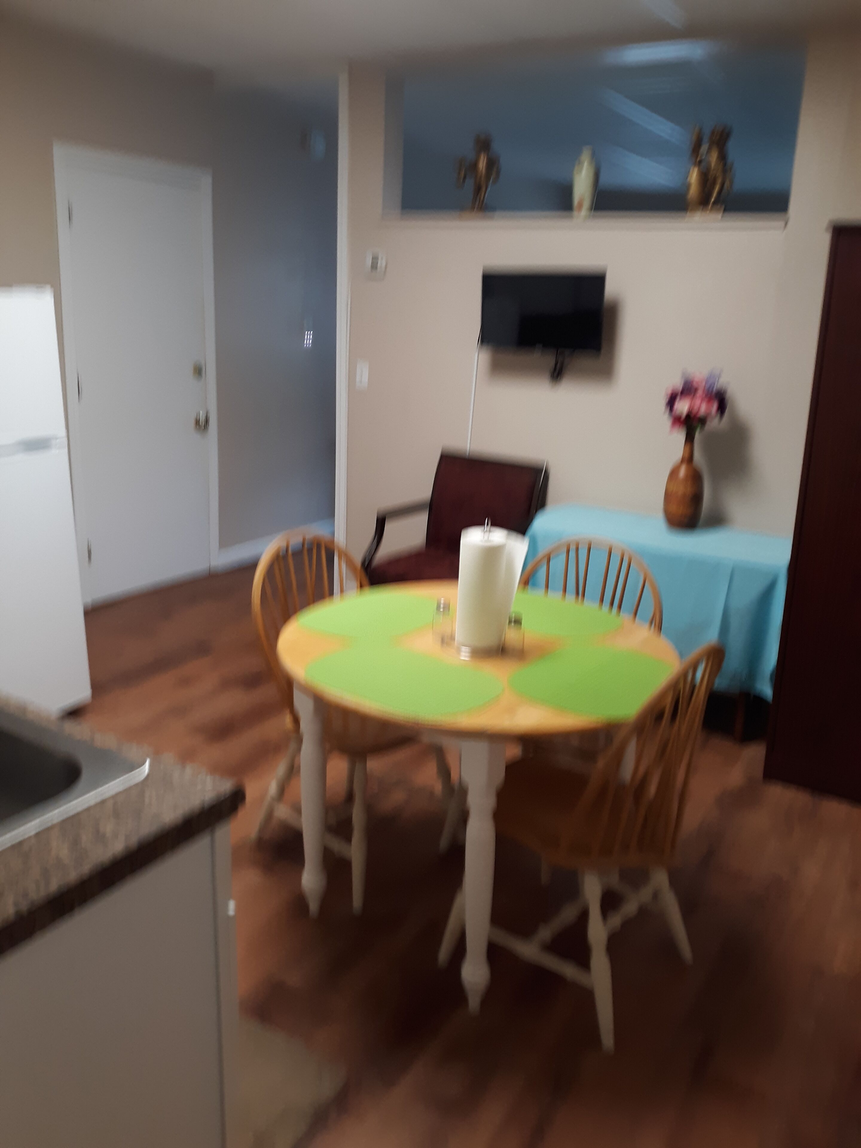 Un comedor con una mesa redonda, sillas, un jarrón con flores y un televisor montado en la pared.