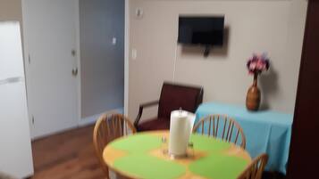 Un comedor con una mesa redonda, sillas, un jarrón con flores y un televisor montado en la pared.