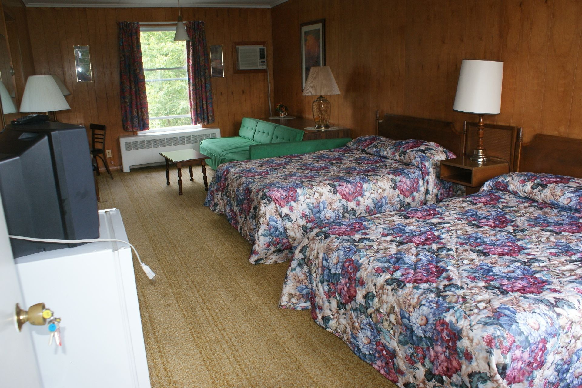 A hotel room with two beds, a green sofa, a desk, and a television.