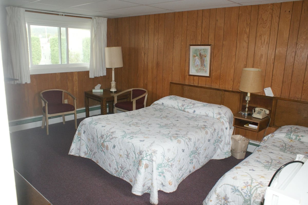 A hotel room with two beds, a desk, a chair, a window with curtains, and a painting on the wall.