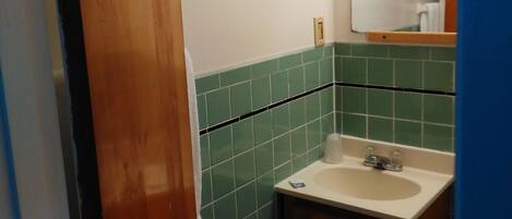 A bathroom with a wooden door, green tiled walls, a white sink, and a mirror above it.