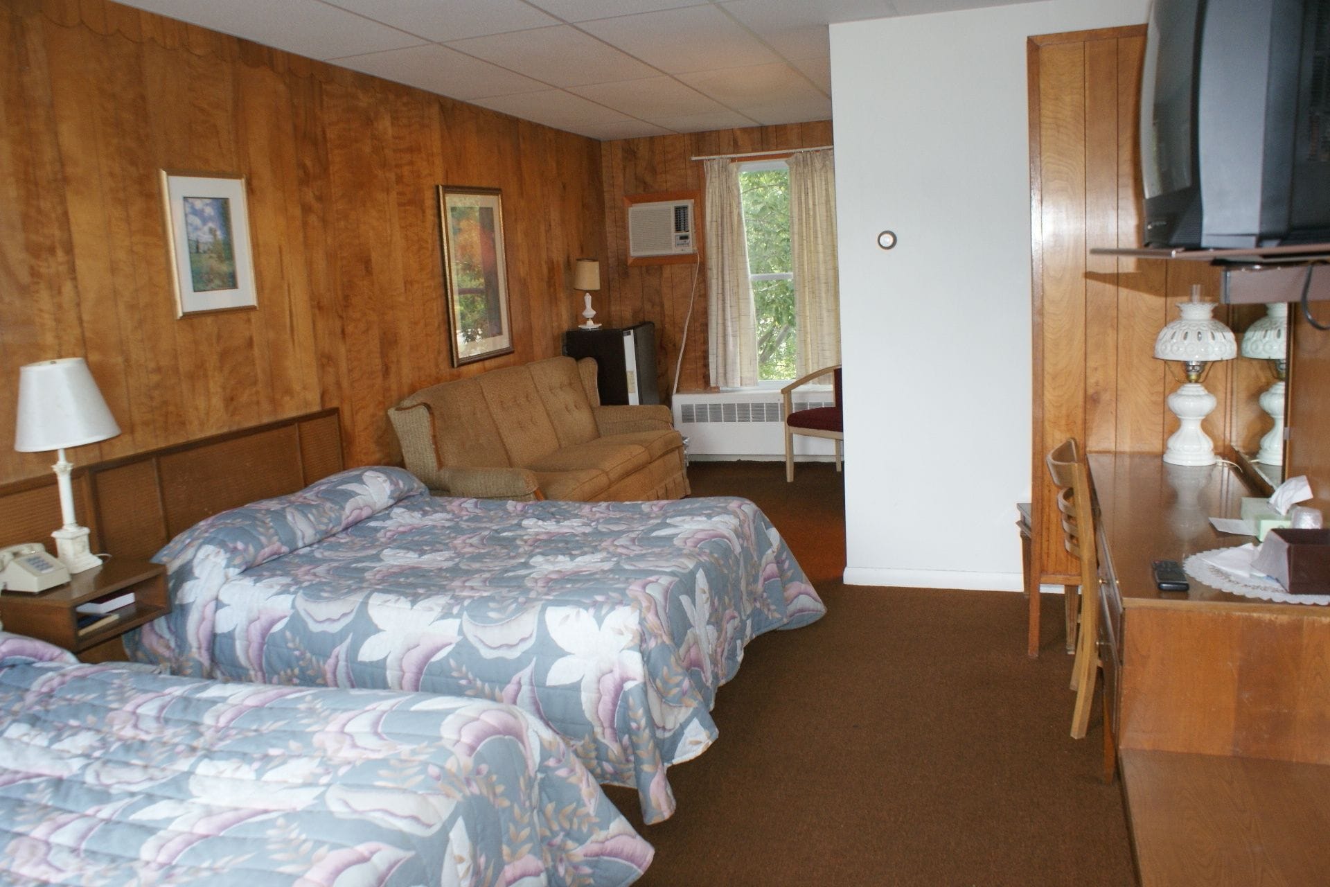A hotel room with two beds, a desk, a chair, a television, and a window with curtains.