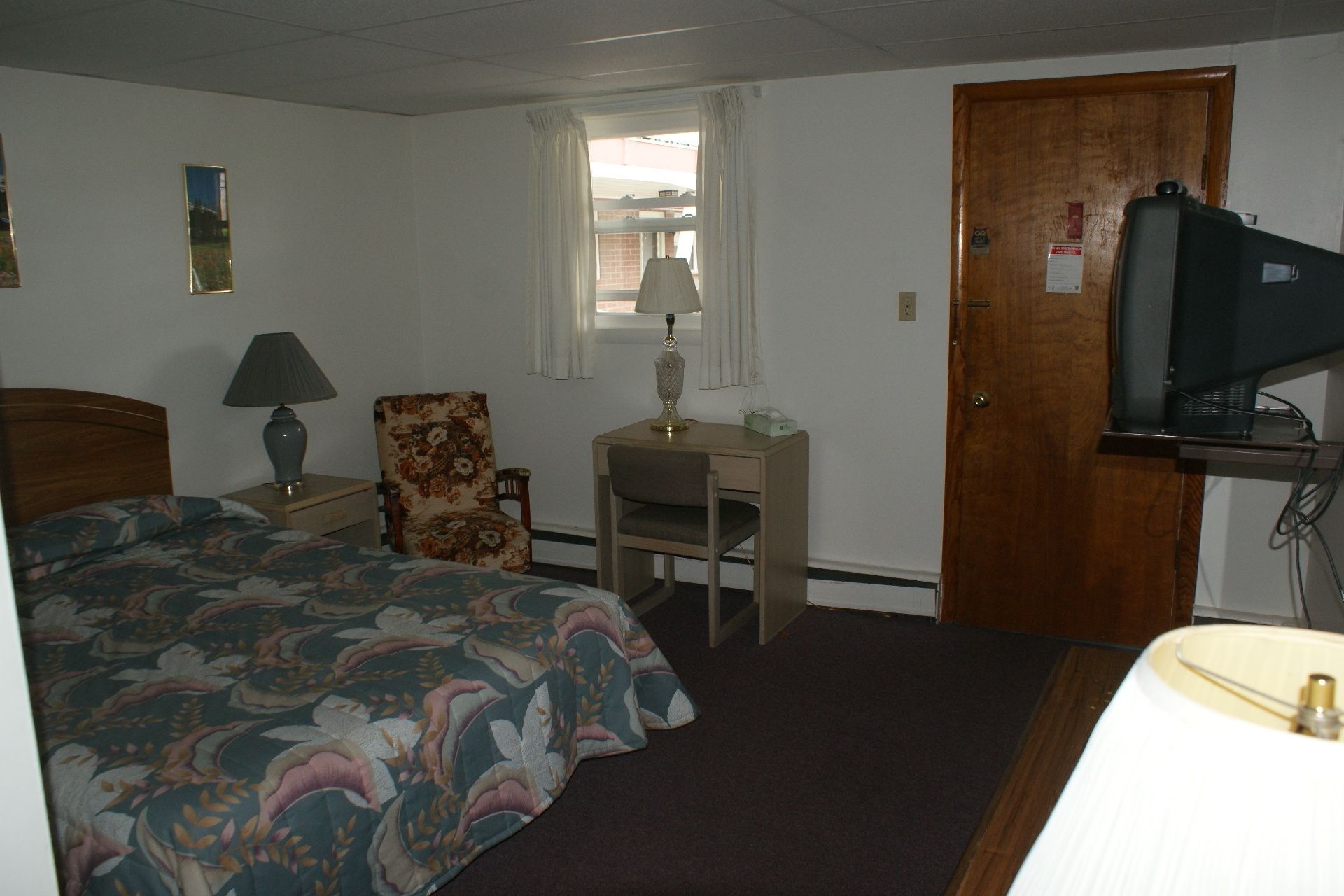 Una habitación de hotel con cama, escritorio, silla, televisor y ventana.