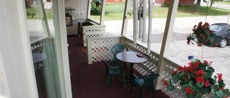 A covered patio area with a table and chairs, a hanging plant, and a view of a red building in the background.