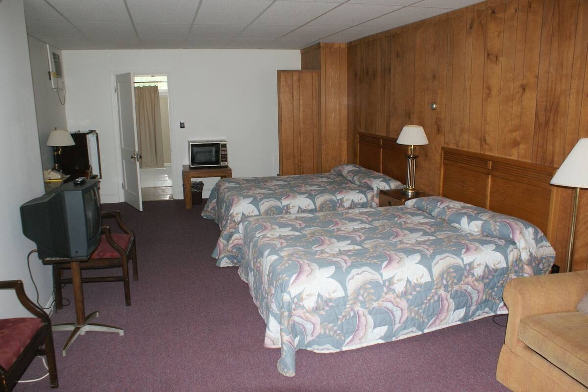 A hotel room with two beds, a television, a small table, and a chair.