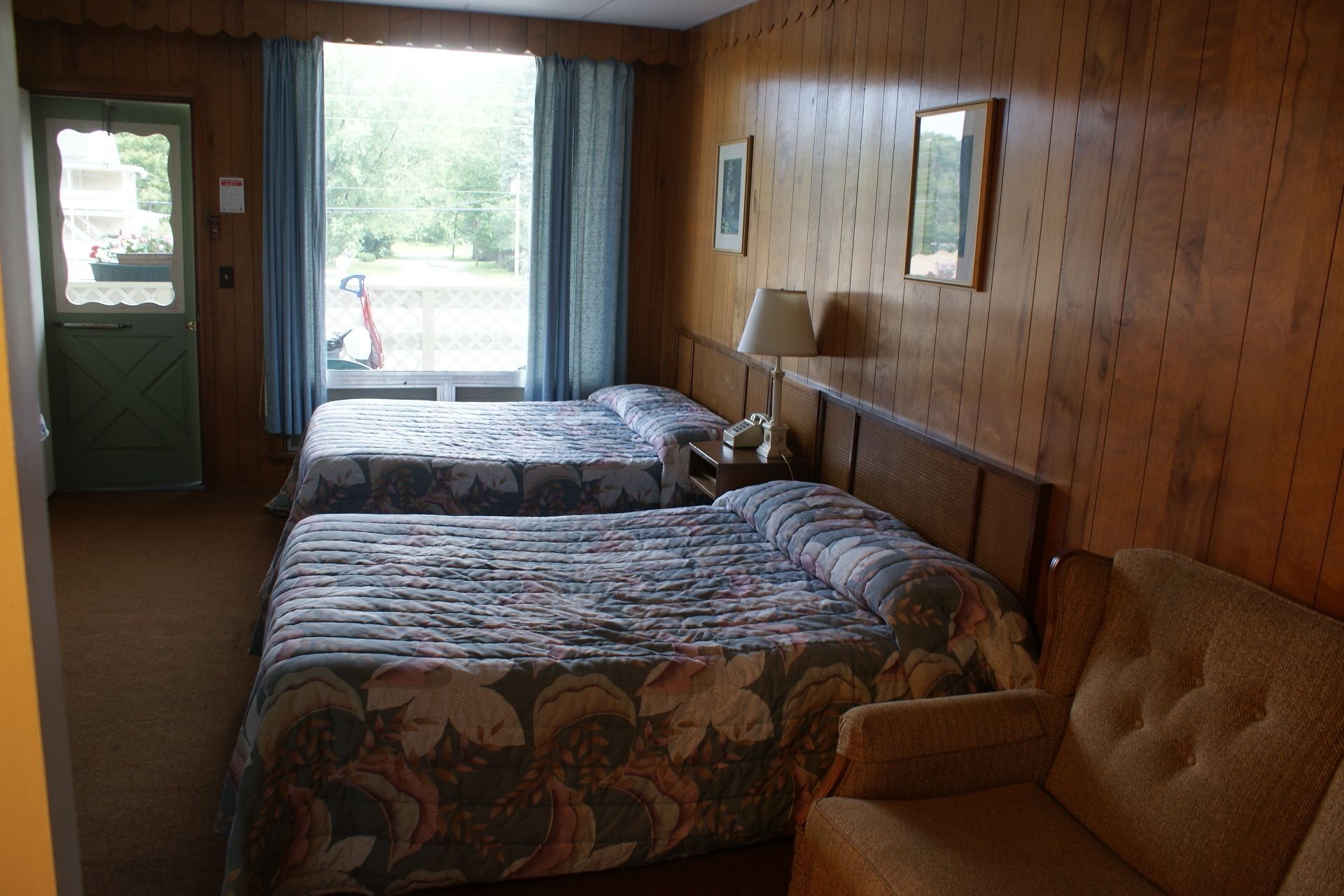 Une chambre d’hôtel avec deux lits, une chaise, une table de chevet avec une lampe et une fenêtre avec des rideaux.