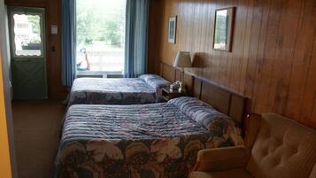 Une chambre d’hôtel avec deux lits, une chaise, une table de chevet avec une lampe et une fenêtre avec des rideaux.