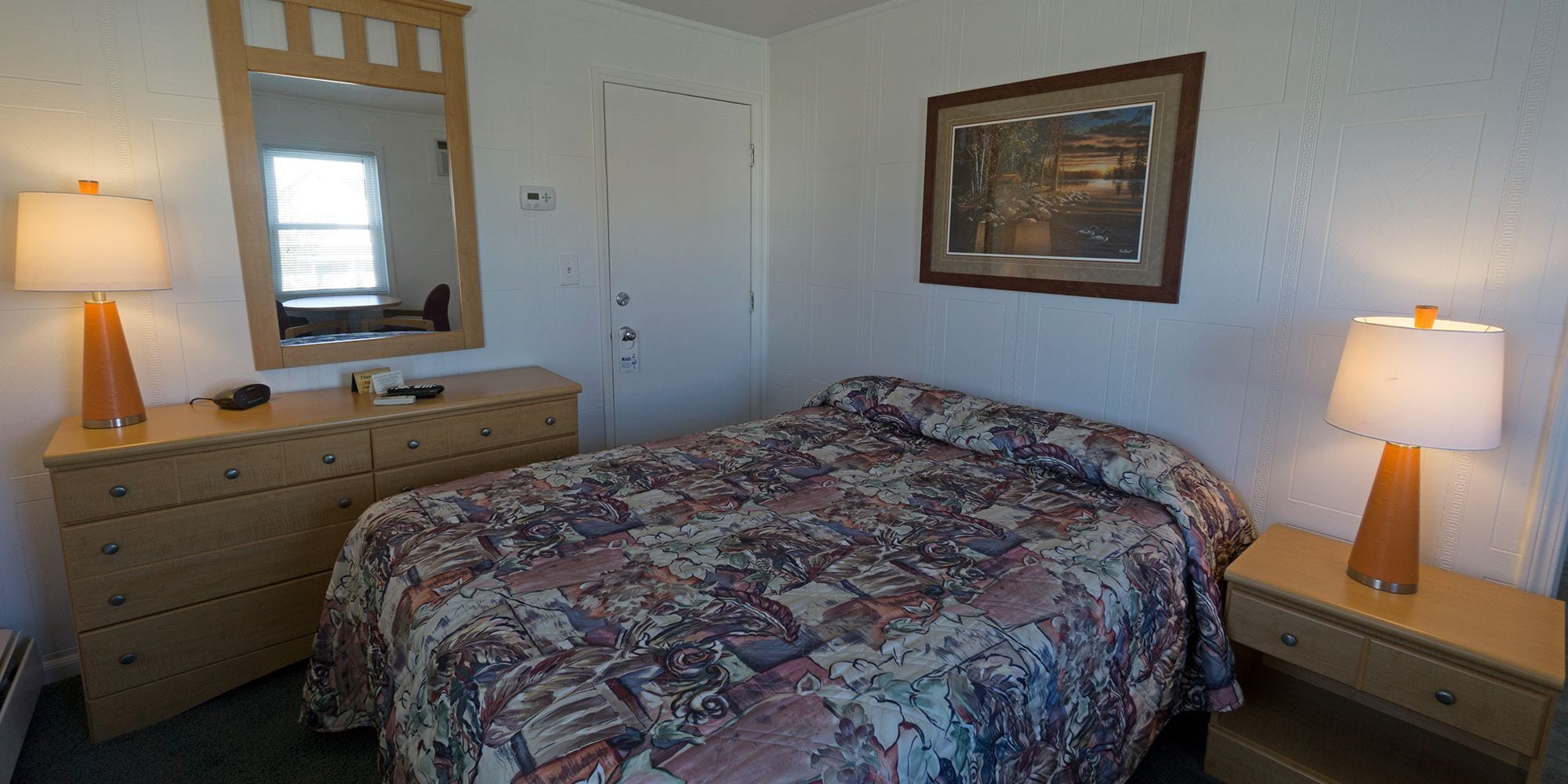 Un dormitorio con cama, cómoda, mesitas de noche, un espejo y un cuadro en la pared.