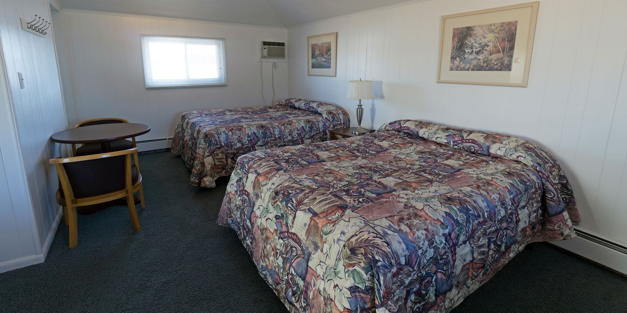 A hotel room with two beds, a small table, and a chair.
