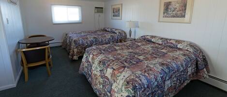 A hotel room with two beds, a small table, and a chair.