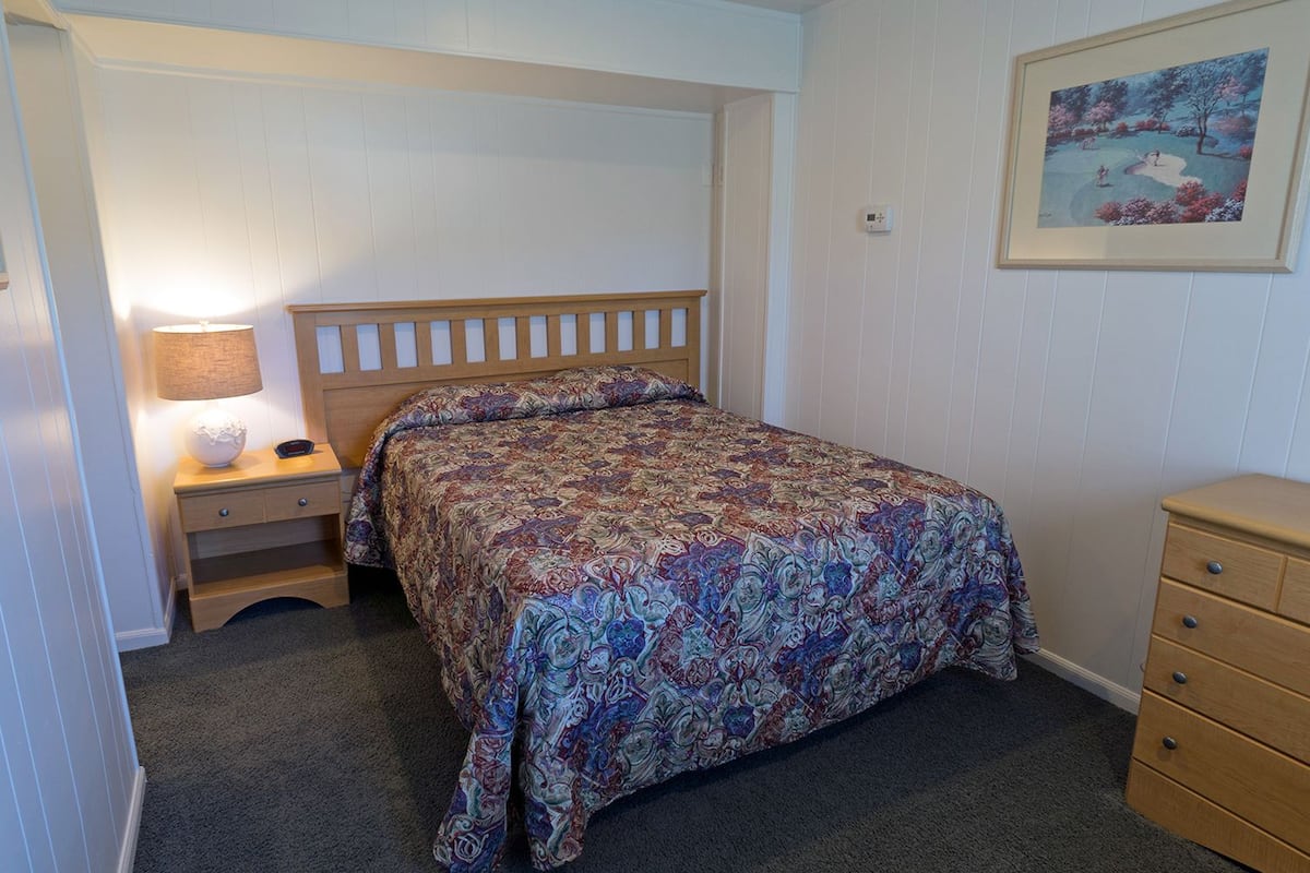 Une chambre à coucher comprenant un lit, une table de chevet, une commode et une lampe.