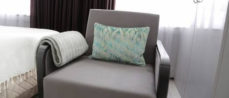 Una camera d'albergo moderna con una poltrona rivestita in grigio, un cuscino decorato e un letto rifatto.