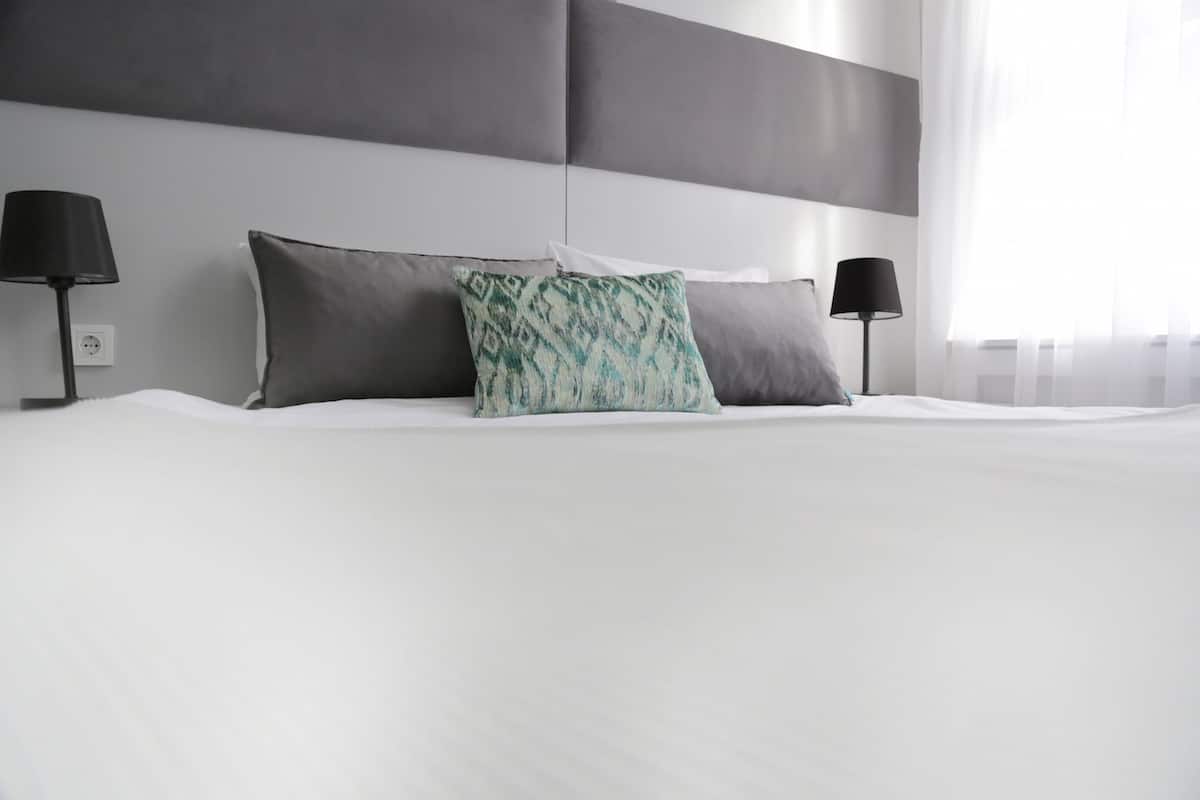 A modern hotel room with a large bed, grey headboard, and two black lamps.