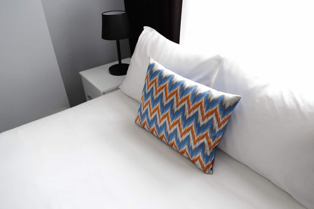 A neatly made bed with a white pillow and a patterned pillow.