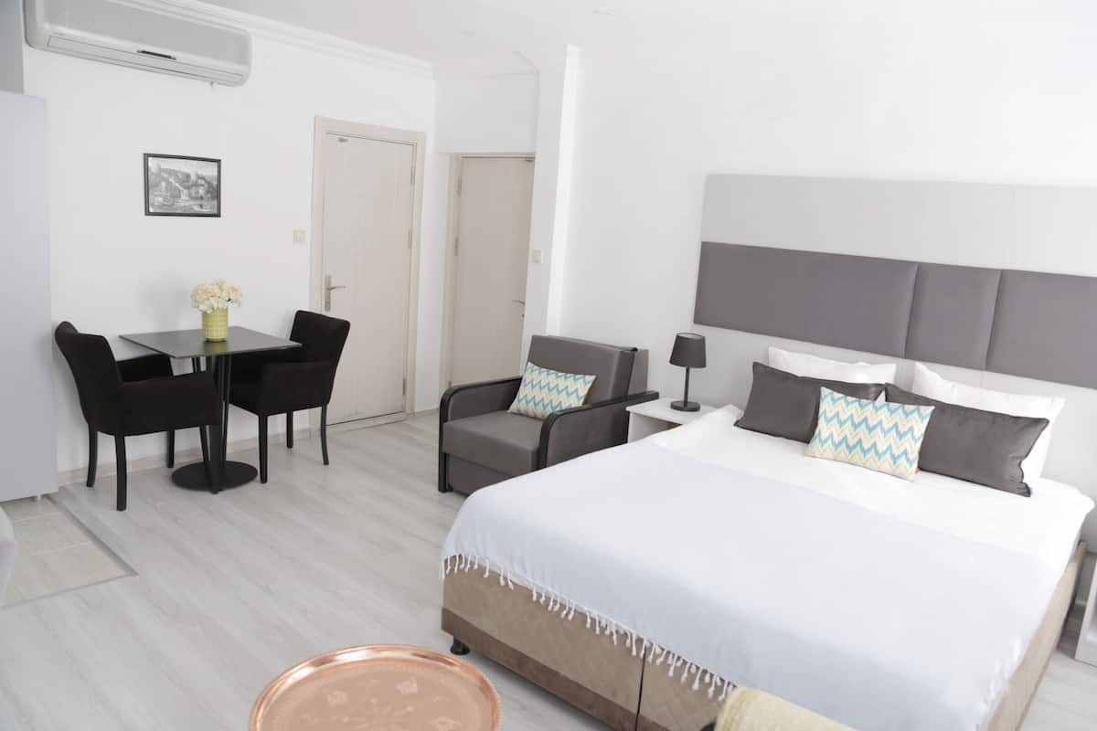A hotel room with a bed, a desk with two chairs, a sofa, and a small table with a vase of flowers.