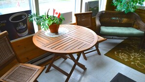 Een ronde houten tafel met een bloempot, rieten stoelen en een gestoffeerde bank in een ruimte met betegelde vloer en een kamerbreed tapijt.