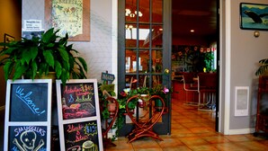 Een restaurantinterieur met een krijtbordmenu, een welkomstbord en een eetgedeelte zichtbaar door een glazen deur.
