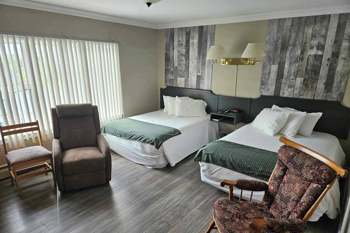 A hotel room with two beds, a chair, a nightstand, and a lamp.
