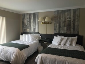 Habitación de hotel con dos camas, una mesita de noche, una lámpara y un aplique de pared.