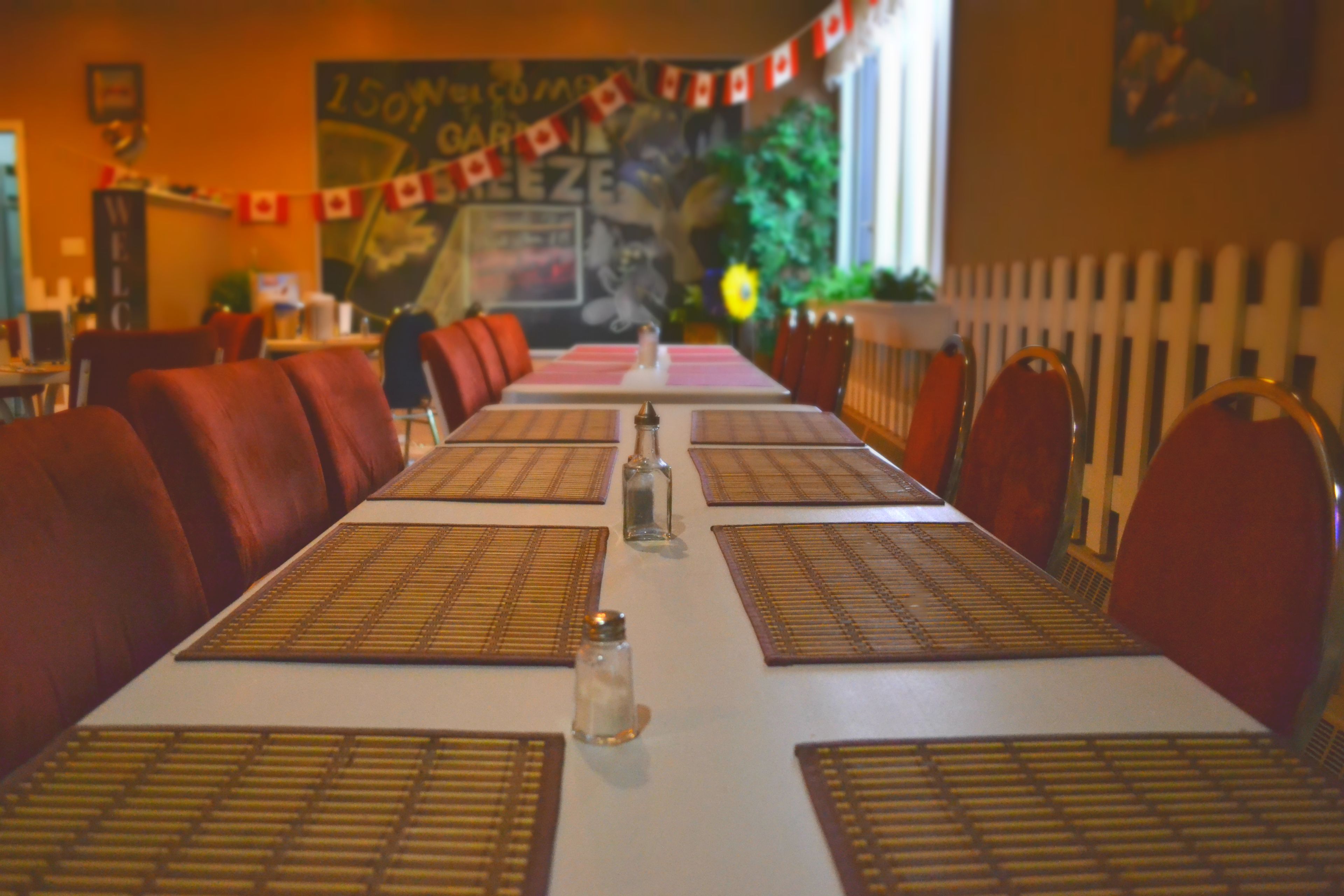 Un restaurant avec une longue table dressée pour le repas, des chaises à revêtement rouge et une banderole accrochée au mur.