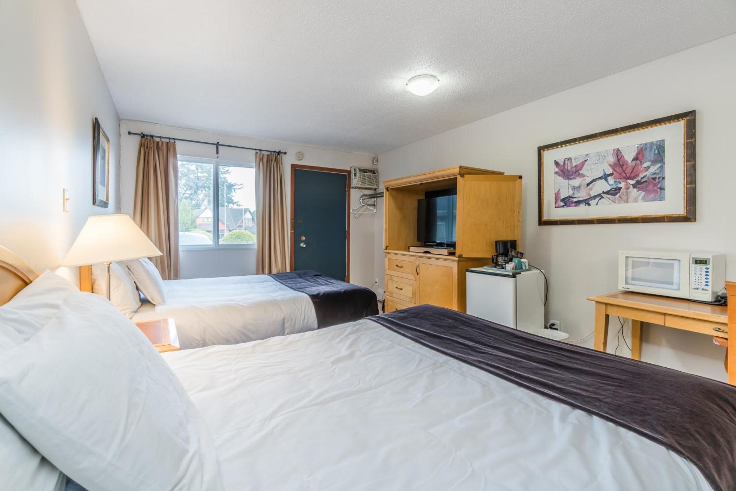 Habitación de hotel con dos camas, un escritorio, televisión, microondas y una ventana con cortinas.