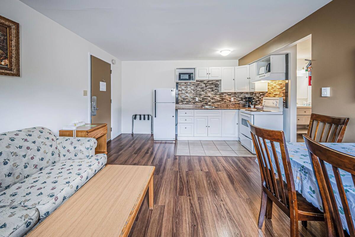 Un espacio habitable compacto con sofá, mesa de comedor y sillas, una kitchenette con microondas y armarios, y piso con diseño.