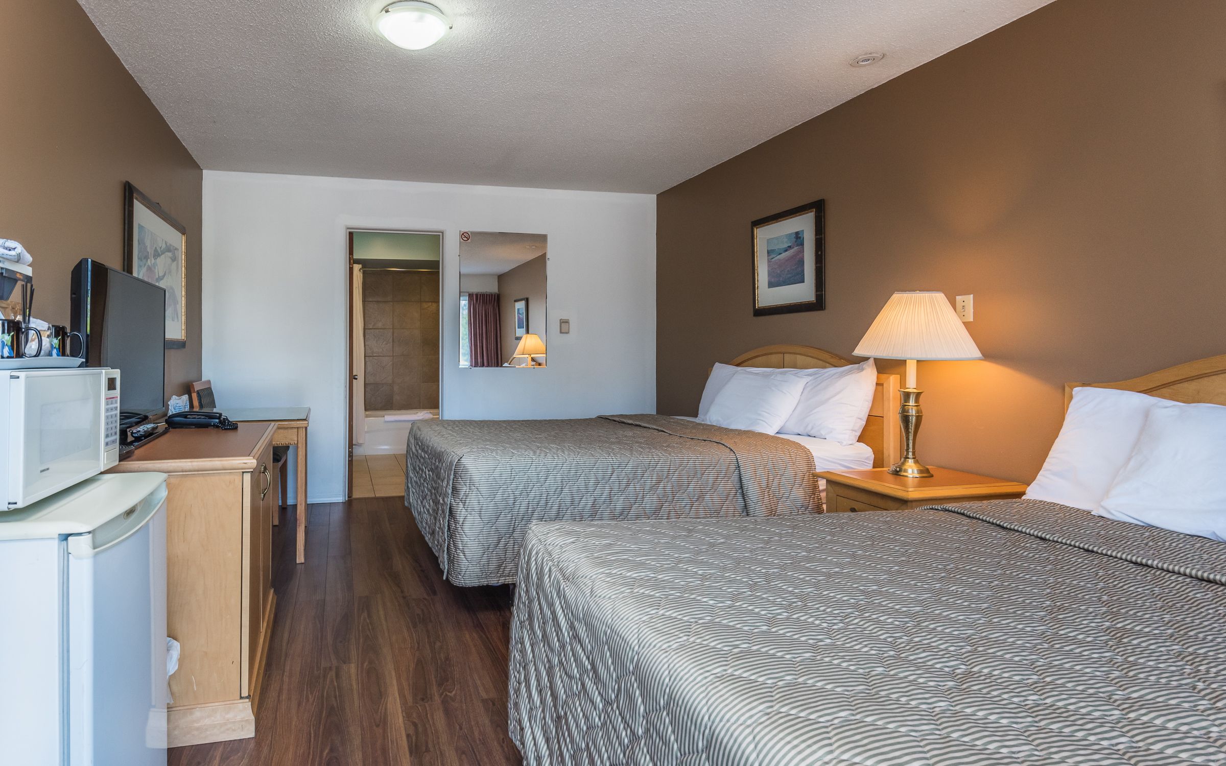 Habitación de hotel con dos camas, un escritorio con microondas, televisor y zona de ducha.