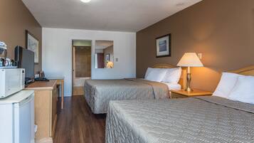 Habitación de hotel con dos camas, un escritorio con microondas, televisor y zona de ducha.