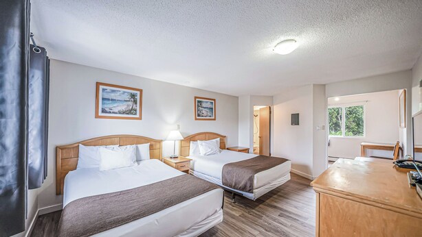 Habitación de hotel con dos camas, cabeceros de madera, mesitas de noche con lámparas y cuadros en las paredes.