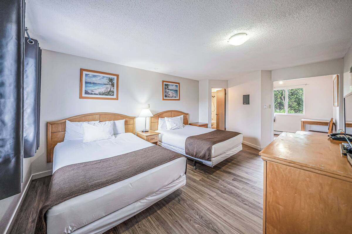 Habitación de hotel con dos camas, cabeceros de madera, mesitas de noche con lámparas y cuadros en las paredes.