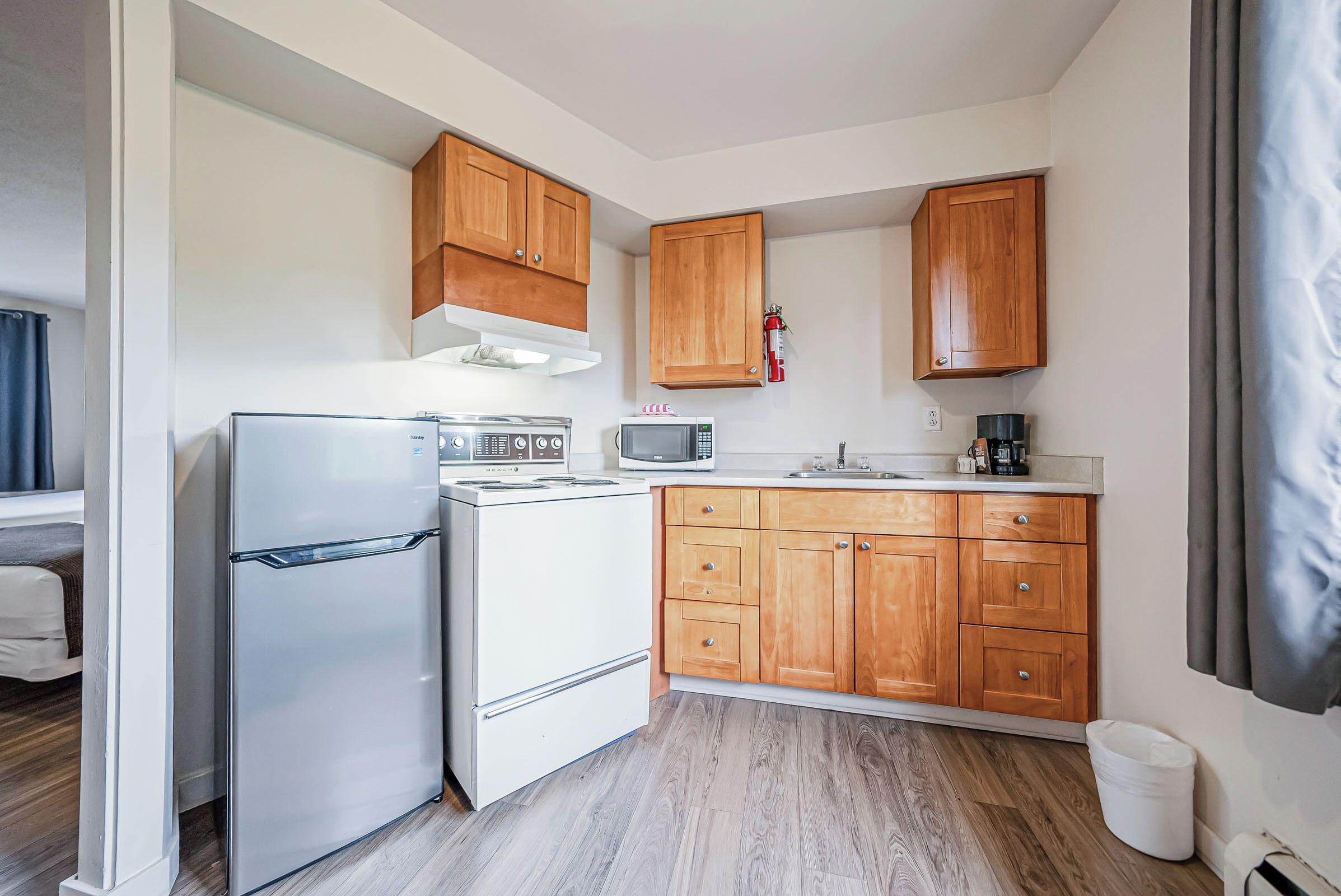 Una cocina compacta con armarios de madera, un refrigerador, un microondas y una estufa.