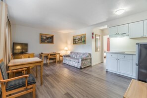 A compact living space with a wooden dining table, a sofa, a TV, a kitchen area with cabinets and a refrigerator.