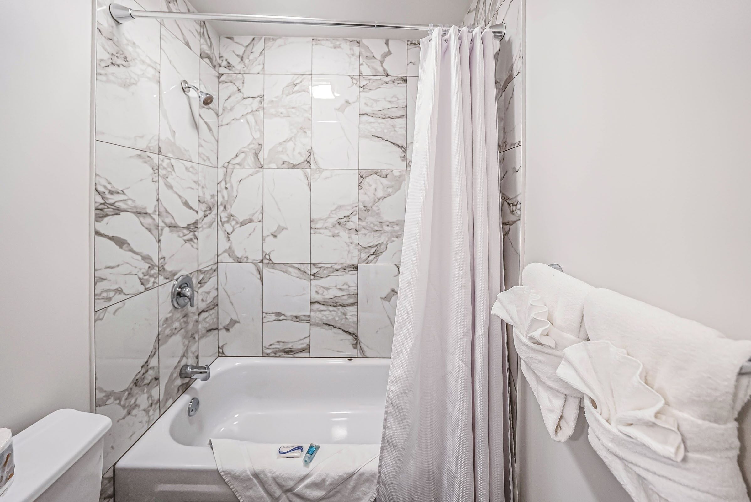 A bathroom with a bathtub, a shower curtain, and a towel rack with towels.