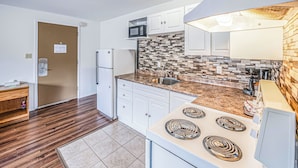 Una cocina moderna con gabinetes blancos, microondas, estufa y salpicadero de azulejos.