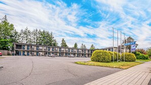 Un motel con estacionamiento, un edificio de varias ventanas y un letrero que indica el nombre del motel.