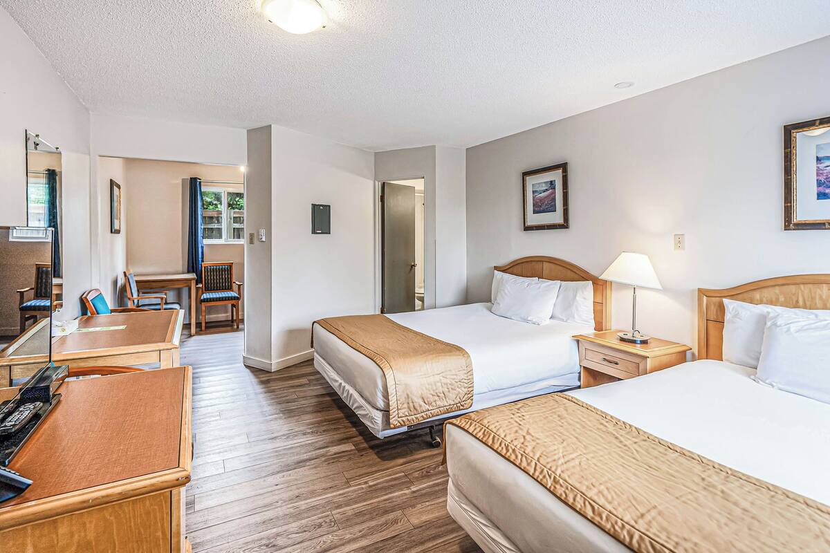 Habitación de hotel con dos camas, un escritorio, una silla y una mesita.