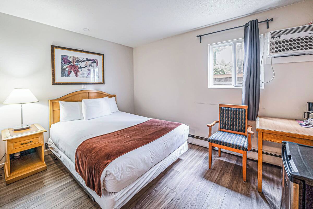 Habitación de hotel ordenada con cama, una silla, una mesa y una ventana con cortinas.