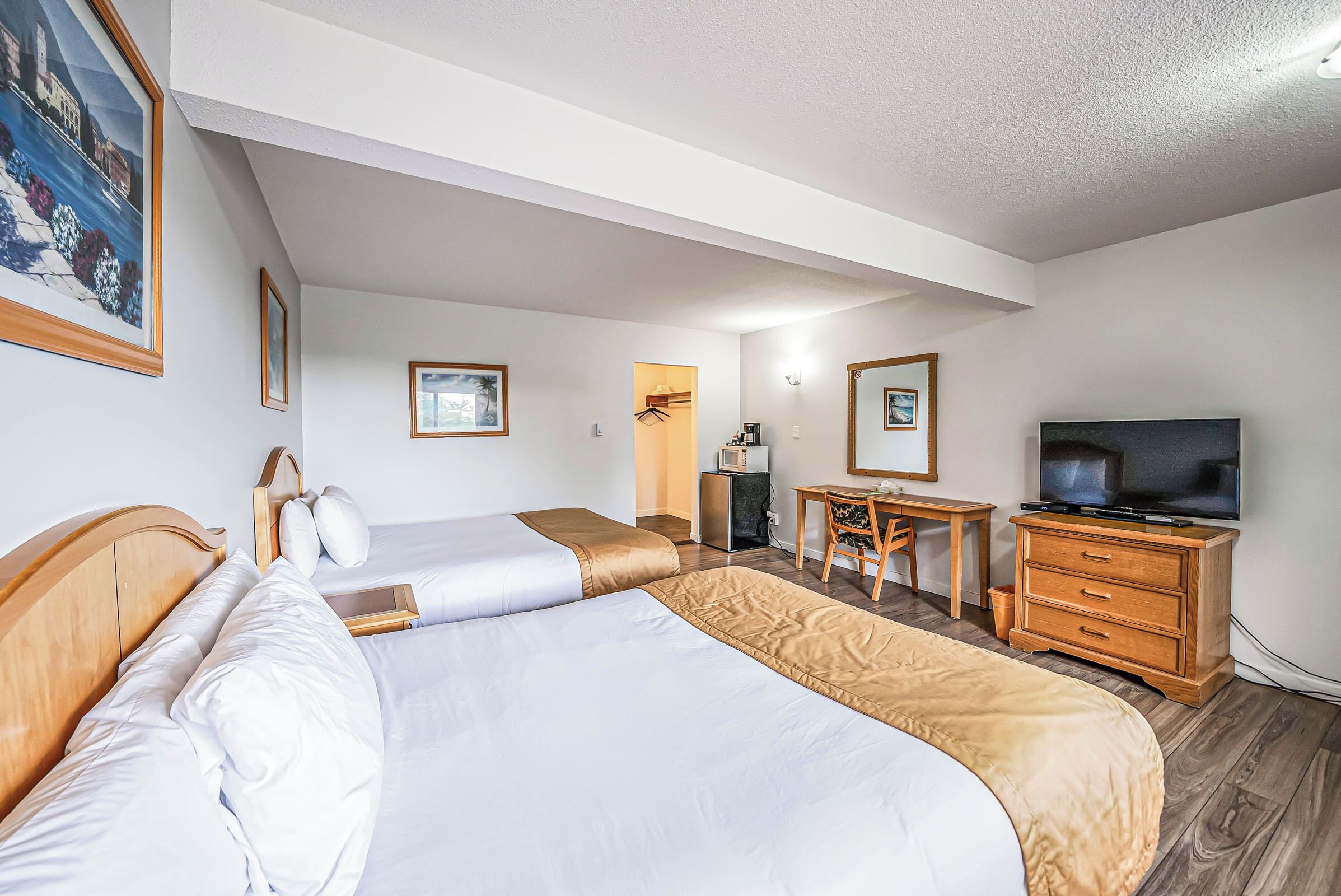 A hotel room with two beds, a desk, a chair, a television, and a mirror.
