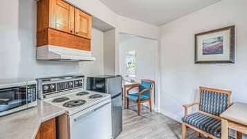 A kitchen with wooden cabinets, a stove, a refrigerator, and a microwave. There is a chair and a table in the dining area.