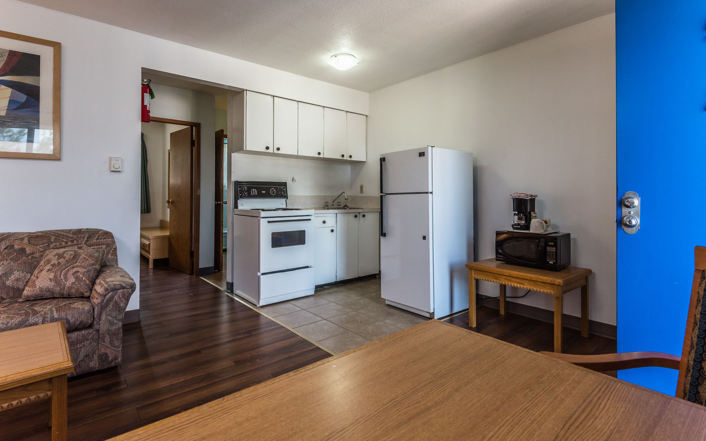 Una cocina compacta con armarios blancos, horno empotrado, refrigerador y microondas sobre una pequeña mesa.