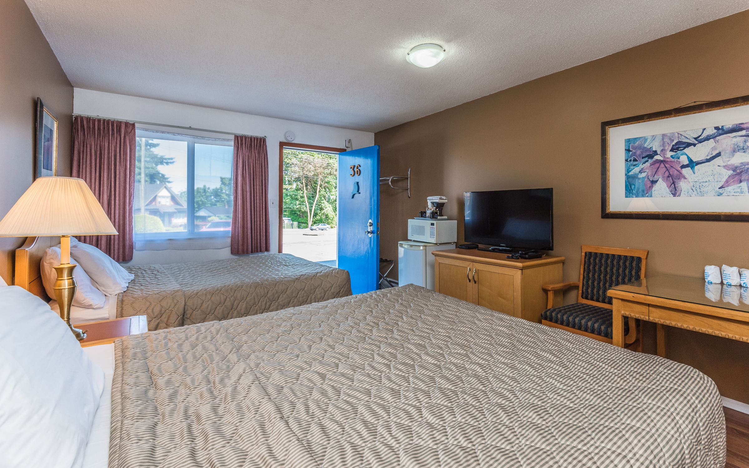 Ett hotellrum med två sängar, en TV, ett skrivbord, en stol, en lampa och en dörr som leder ut.